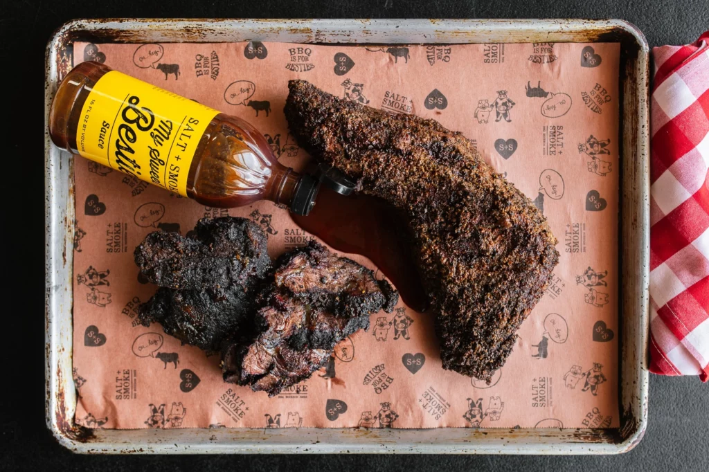 bbq sauce spilled on a tray next to brisket and pork