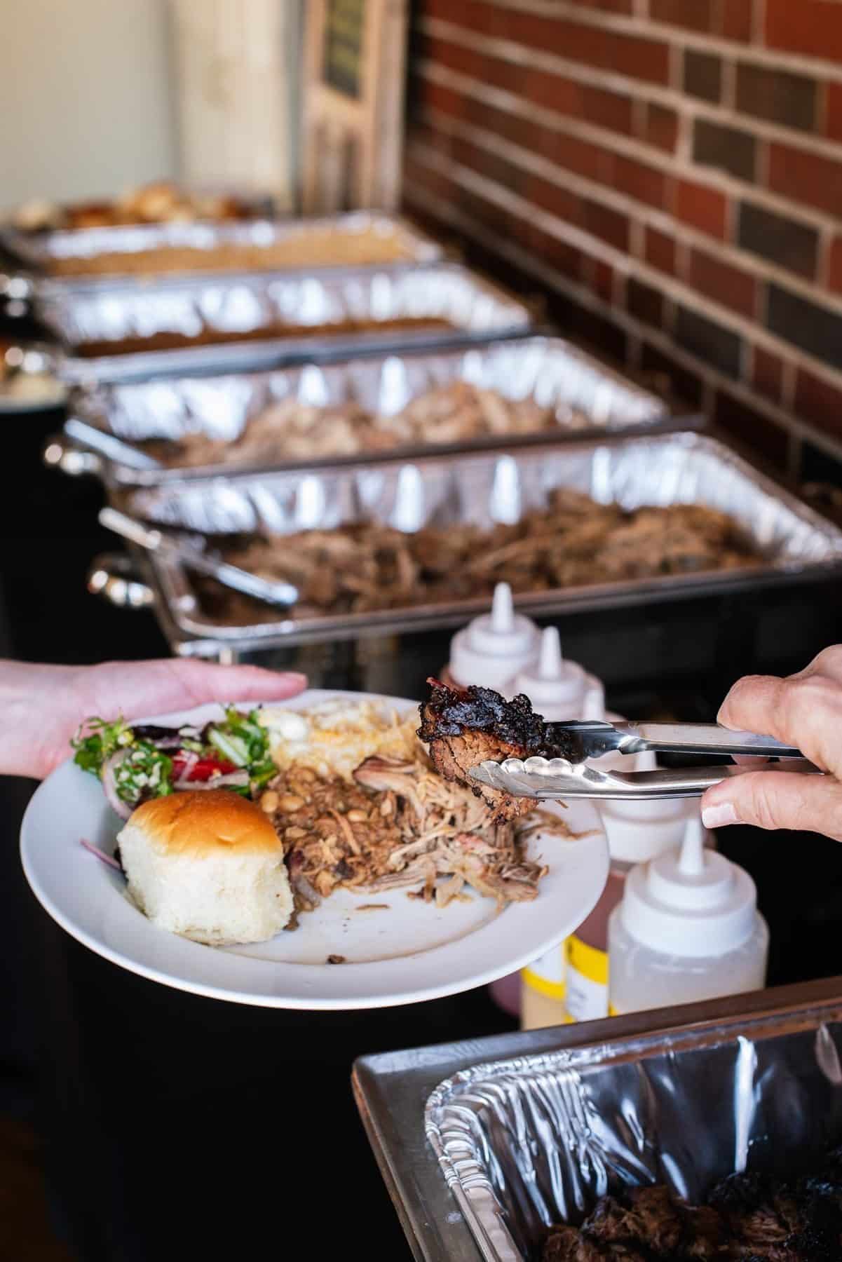 Corporate Catering 2 A guest is served burnt ends from a Salt + Smoke buffet line