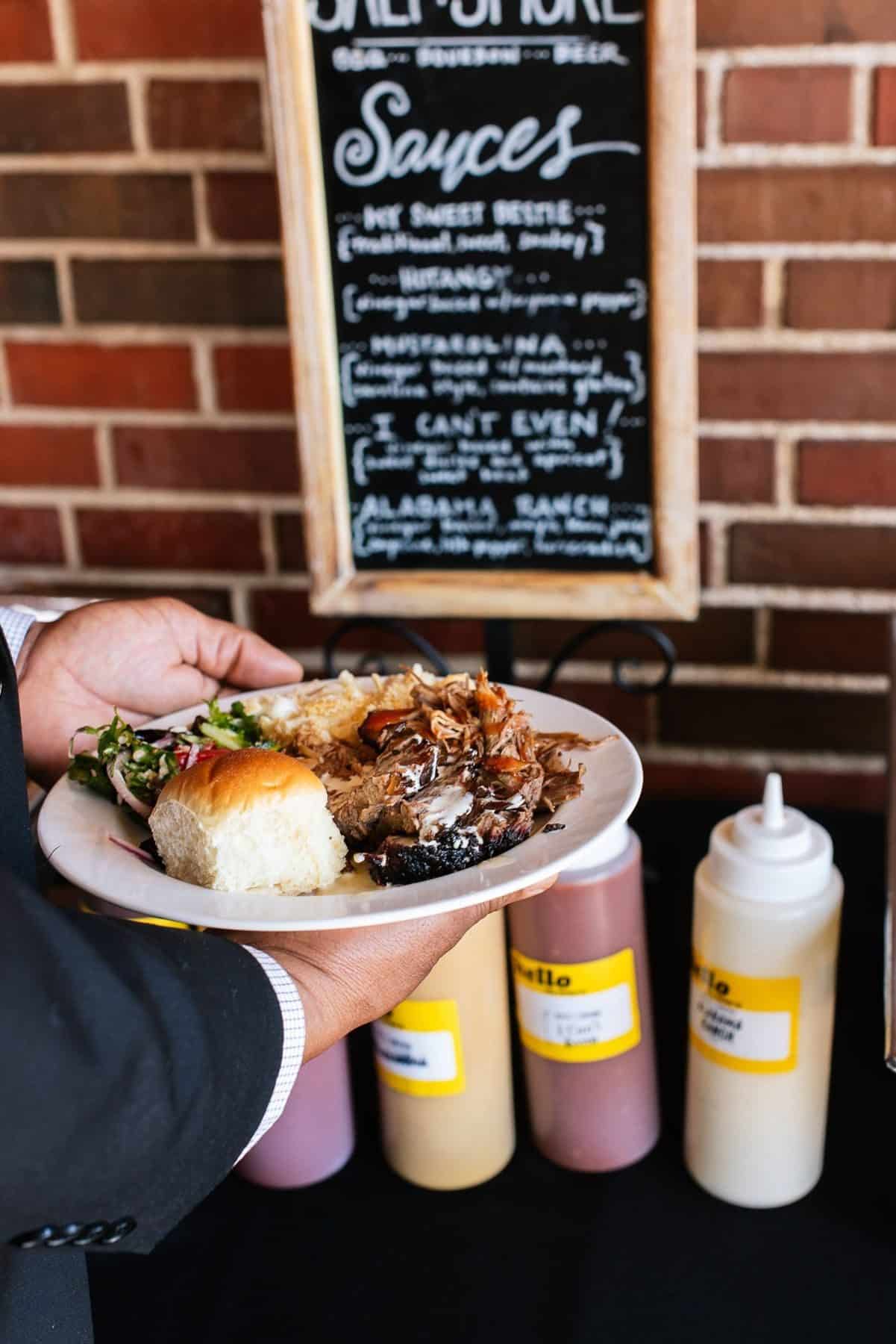 Catering 12 A guest holds a plate of BBQ in front of the Salt + Smoke sauce bar