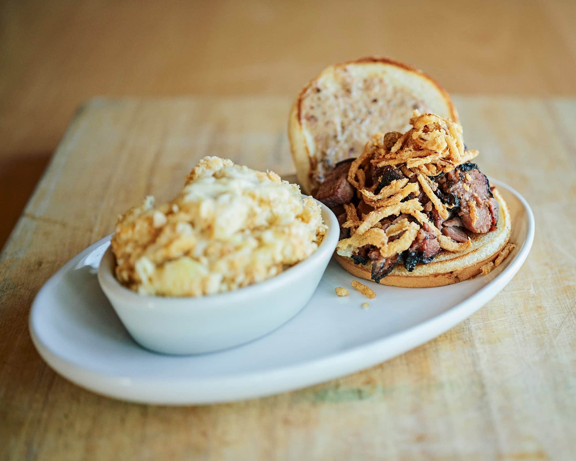 Boxed Lunches 1 A smoked brisket sandwich topped with crispy fried onions on a toasted bun, with a side of white cheddar cracker mac