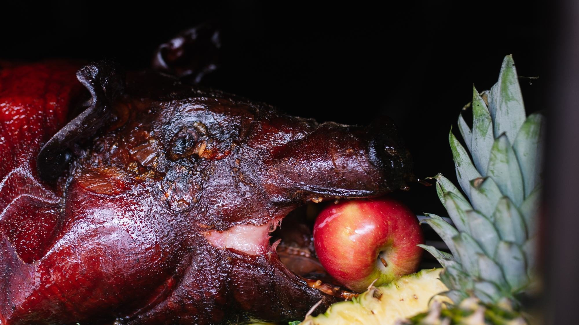 Whole Hog Roast 1 A whole smoked hog with an apple in its mouth, garnished with kale and pineapple