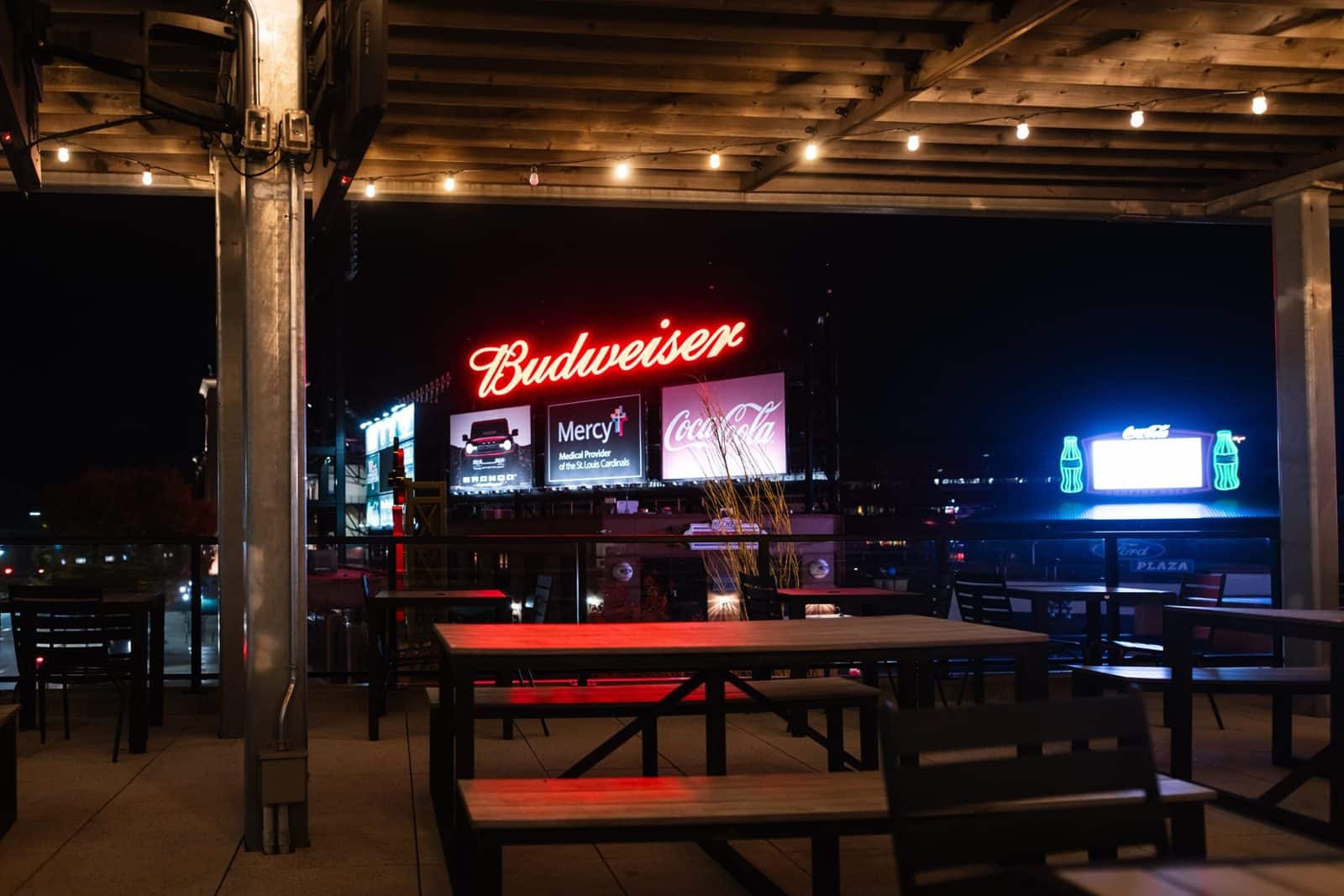 Book an event space 6 The covered Ballpark Village patio at night, with string lights and picnic tables