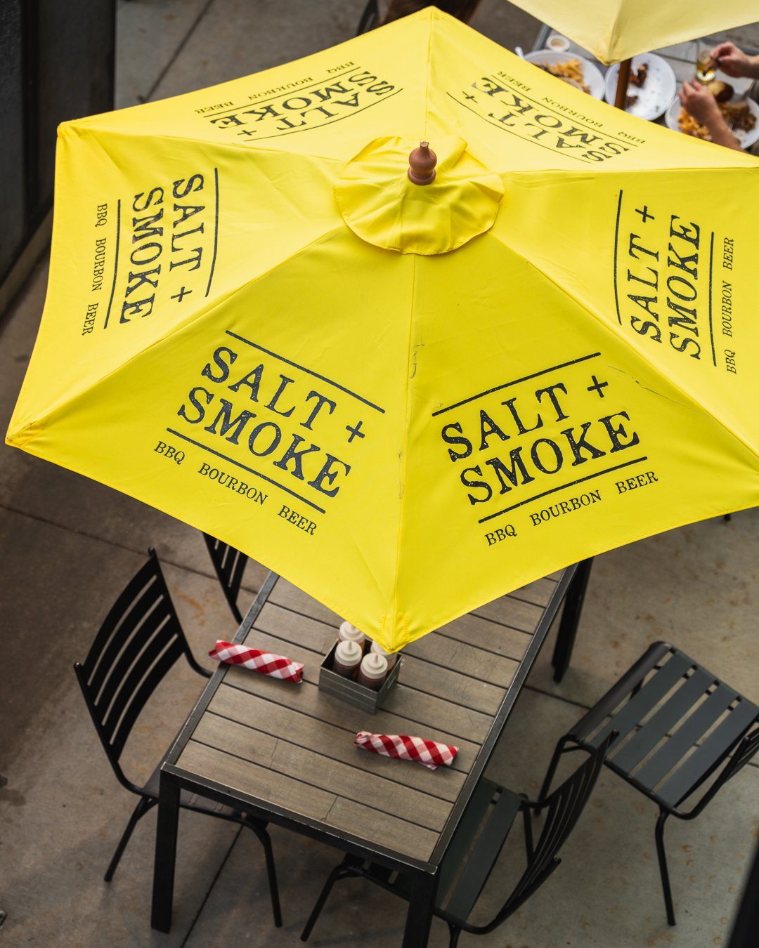 Ballpark Village 12 A yellow Salt + Smoke umbrella over a patio table
